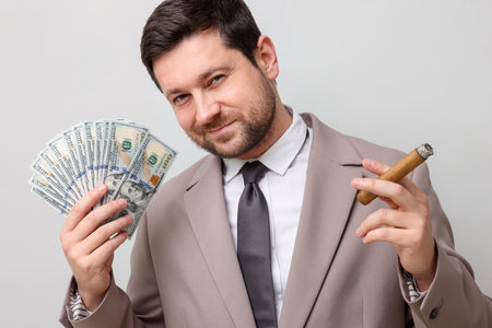 Greedy banker with dollar banknotes smoking cigar on grey backgroundの写真素材