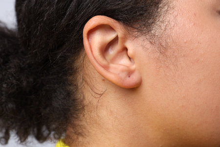Young woman with pierced ear on light grey background, closeup
