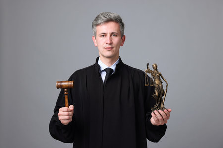Judge with mallet and statue of Lady Justice on grey background