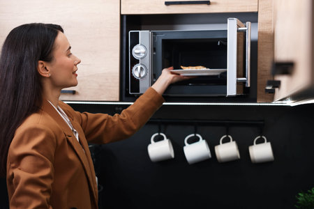 Woman putting plate with lunch into microwave indoors