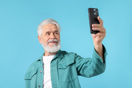 Elderly man taking selfie on light blue backgroundの写真素材
