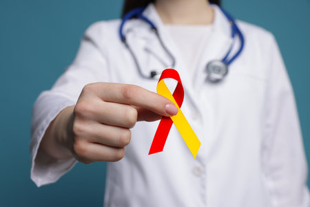 World Hepatitis Day. Doctor with yellow-red awareness ribbon on teal background, closeupの写真素材