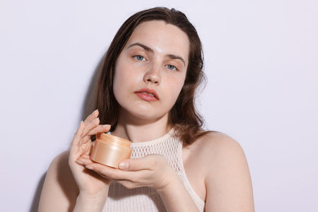 Portrait of beautiful woman with jar of skincare product on light background, closeupの写真素材