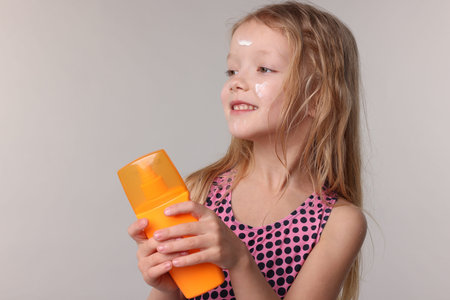 Smiling little girl with bottle of sun protection product on grey backgroundの写真素材
