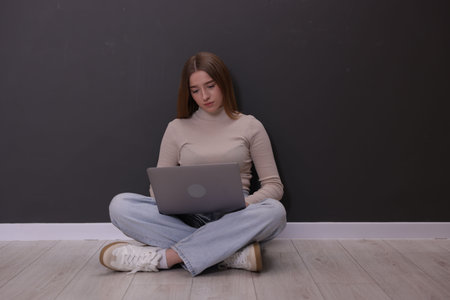 Cyber bullying. Upset teenage girl with laptop on floor indoors