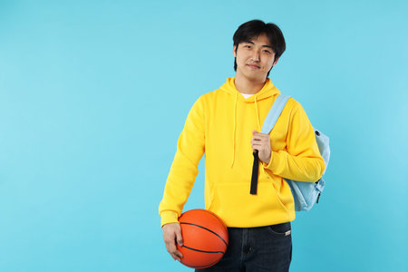 Student with basketball ball and backpack on light blue background, space for textの写真素材