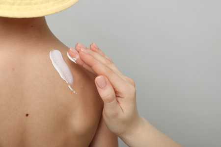 Mother applying sun protection cream onto her son's skin on light grey background, closeup. Space for textの写真素材