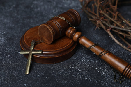 Crown of thorns and judge's gavel with cross on dark textured background, closeup