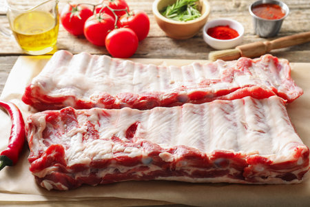Raw pork ribs, spices and tomatoes on wooden table, closeupの写真素材