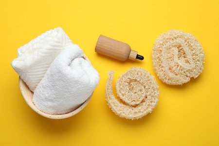 Natural loofah sponges, cosmetic product and towels on yellow background, flat layの写真素材