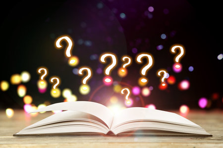 Question marks above open book on table against black background with blurred lights