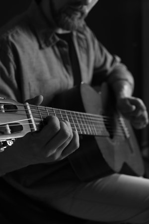 Man playing guitar on dark background, focus on hand. Black and white effect
