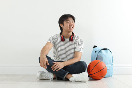 Happy student with basketball ball and backpack on floor indoorsの写真素材