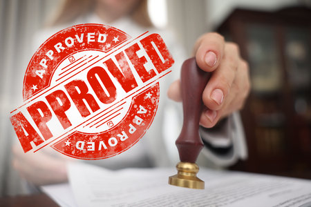 Woman stamping document at table and red stamp Approved