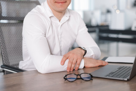 Man with laptop and glasses at wooden desk in office, closeupの写真素材