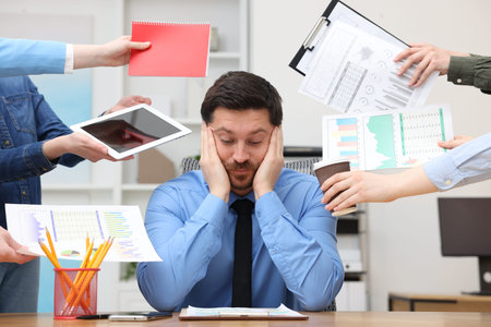 Man overwhelmed by different requests from colleagues at desk in office