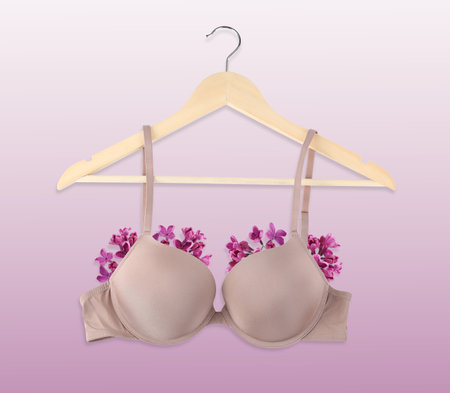 Beautiful bra with lilac flowers on wooden hanger against gradient backgroundの写真素材
