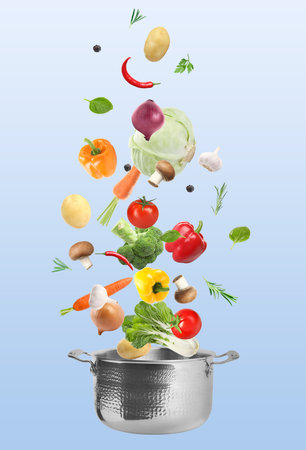Fresh vegetables falling into saucepan against light blue gradient backgroundの写真素材