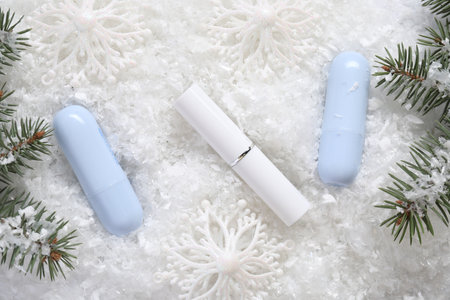 Moisturizing lip balms, Christmas decor and fir tree branches on artificial snow, flat lay. Winter careの写真素材
