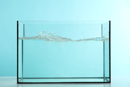 Glass aquarium with splashing water on table against light blue backgroundの写真素材