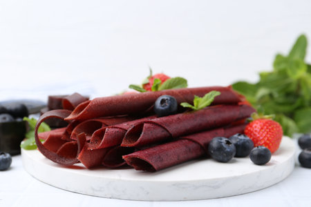 Tasty fruit leather rolls, strawberries, blueberries and mint on white table, closeupの写真素材