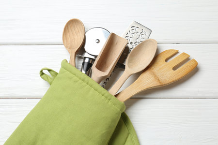 Different kitchen utensils in oven mitten on white wooden table, top viewの写真素材