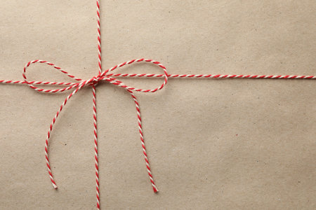 Gift wrapped in kraft paper and bow as background, top view