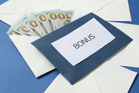 Envelopes with word Bonus and money on blue background, closeup