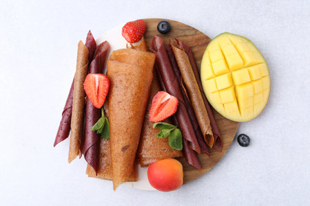 Delicious fruit leather rolls, mint, mango, apricot and berries on light table, flat layの写真素材