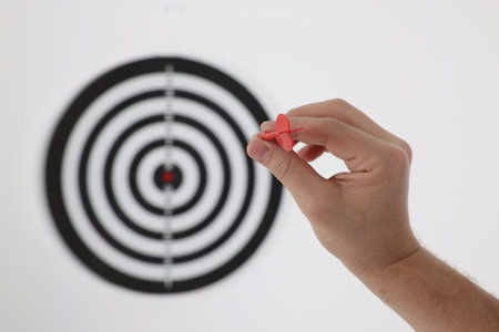 Targeting. Man with arrow aiming at dart board on light background, closeupの写真素材