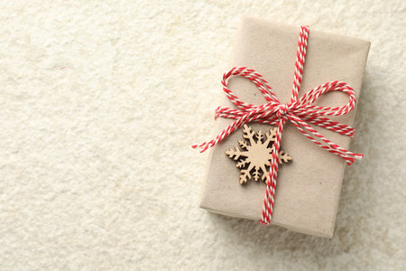 Gift wrapped in kraft paper with bow and ornament on white textured table, top view. Space for textの写真素材