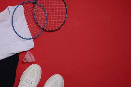Sportswear, sneakers, badminton rackets and shuttlecock on red background, flat lay. Space for text