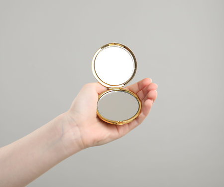 Woman holding open pocket mirror on grey background, closeupの写真素材