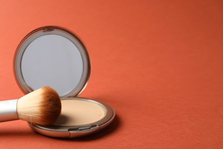 Open face powder with mirror and brush on coral background, closeup. Space for text