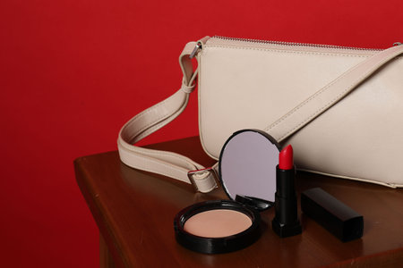 Open face powder with mirror, lipstick and bag on wooden stool against red background, closeupの写真素材