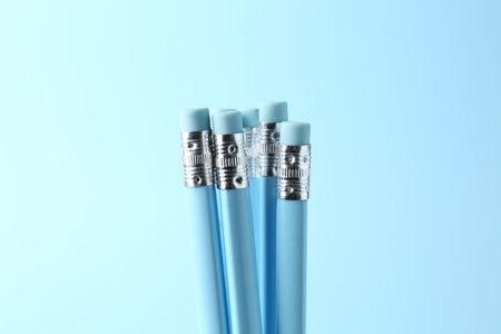 Pencils with erasers on light blue background, closeup