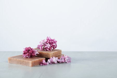 Soap bars and lilac flowers on grey table against light background. Space for textの写真素材