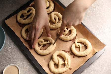 Woman cutting uncooked pretzel at grey table, above view