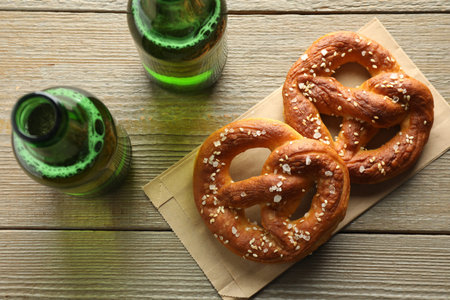 Tasty pretzels and bottles of beer on wooden table, flat lay
