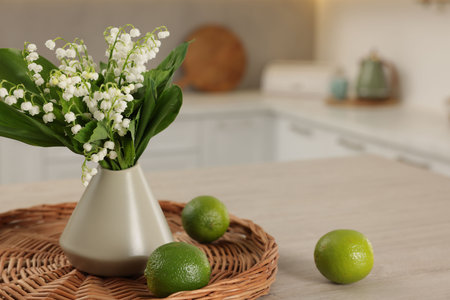 Bouquet of beautiful lily-of-the-valley in vase and limes on wooden table in kitchen, closeup. Space for textの写真素材