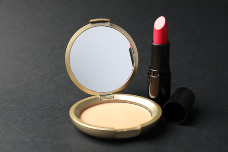 Open face powder with mirror and lipstick on black background, closeup