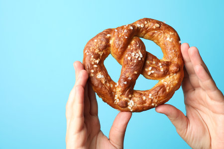 Woman with tasty pretzel on light blue background, closeup