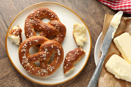 Tasty pretzels with salt and butter on wooden table, flat lay
