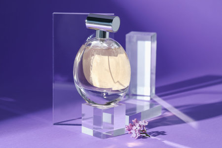 Stylish presentation of perfume bottle and lilac flowers on purple background, closeup