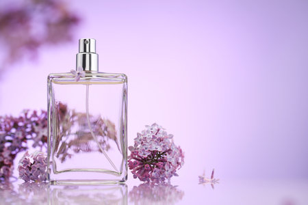 Bottle of perfume and lilac flowers on mirror surface against violet gradient background, selective focus. Space for textの写真素材