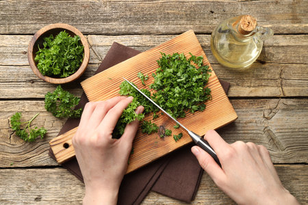 Woman cutting parsley at wooden table, top viewの写真素材