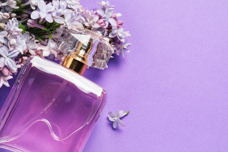 Bottle with perfume and lilac flowers on violet background, above view. Space for textの写真素材