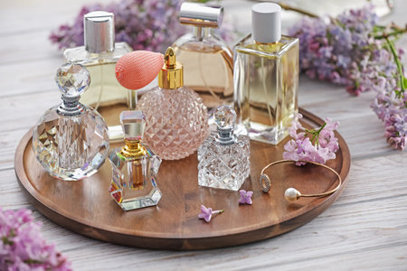 Bottles of perfumes and lilac flowers on white wooden table, closeup