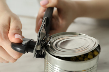 Woman opening tin with can opener at white table, closeupの写真素材