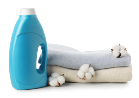 Bottle of fabric softener, stacked clothes and cotton flowers isolated on whiteの写真素材